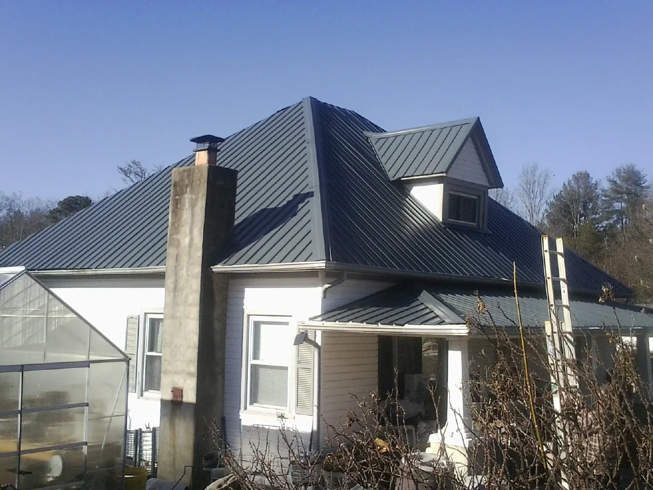 Dark blue standing seam metal roof on a white farmhouse with dormer — Slate & Tile Roof Repair by Roofing Brothers in Palisades Park