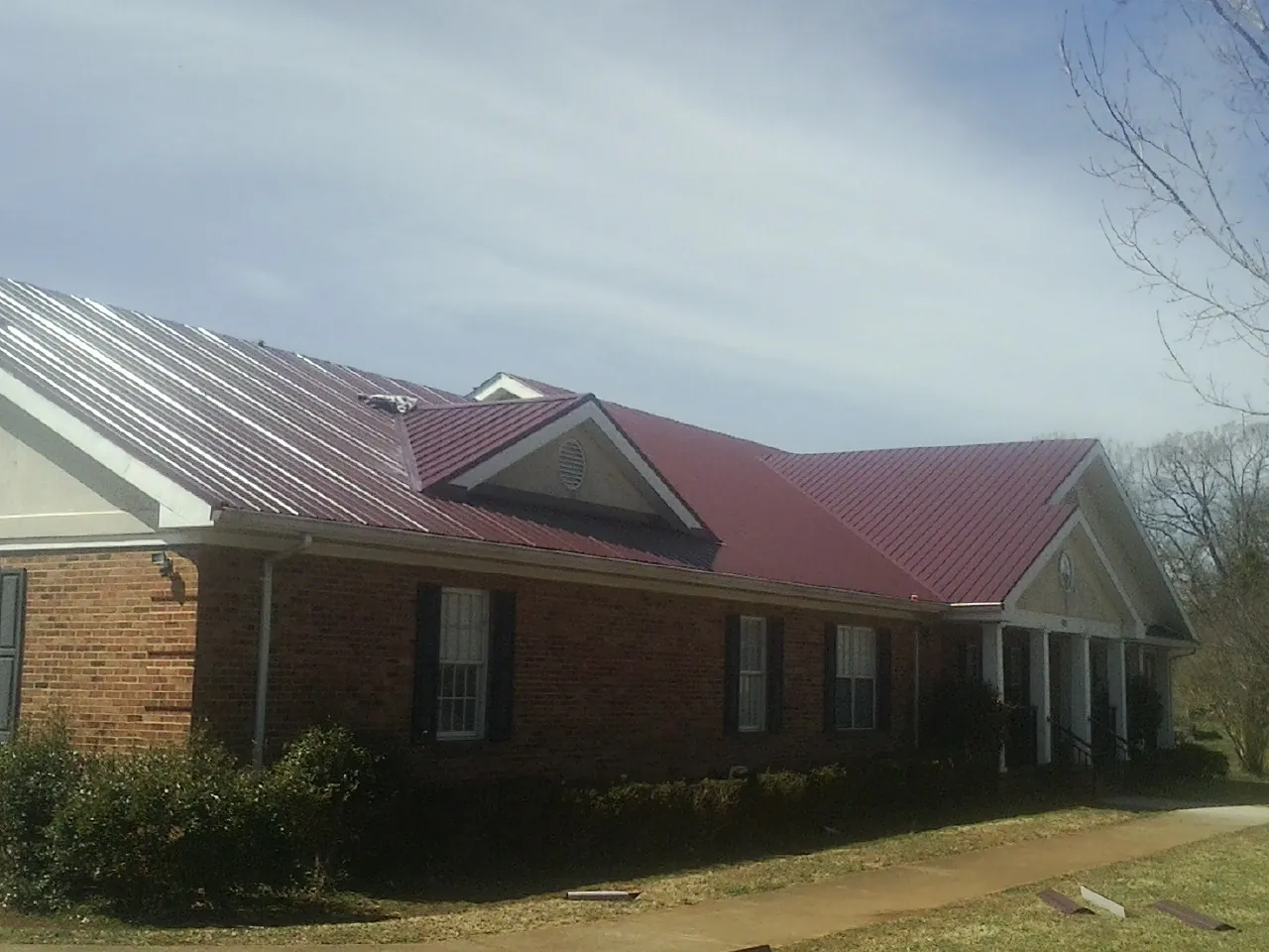 Red metal roof with gabled entries on a long brick building, from a Hail Damage Roof Repair job in Palisades Park