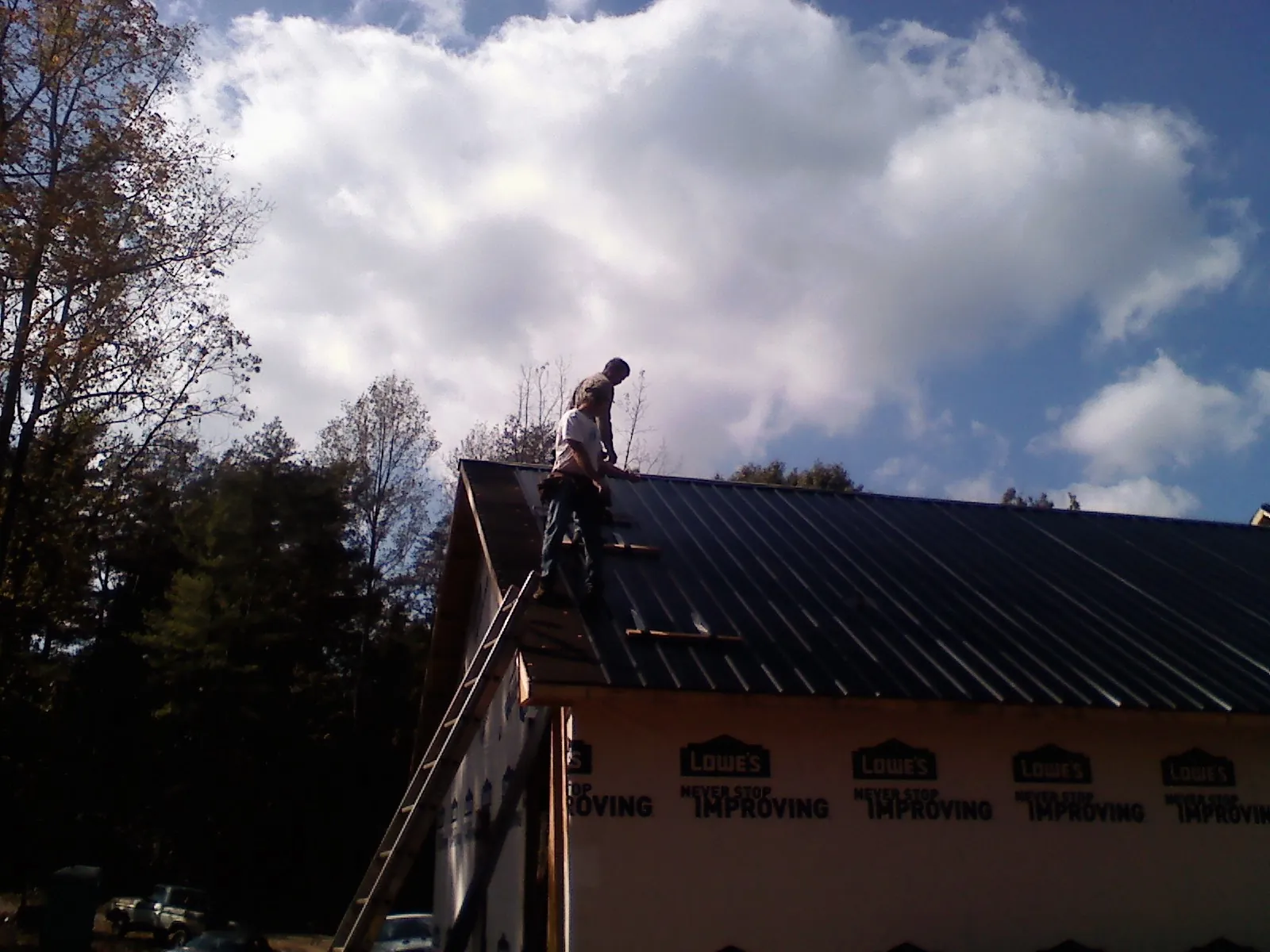Roofer fastening dark metal panels high against a cloudy sky, from a Roof Inspection job in Palisades Park