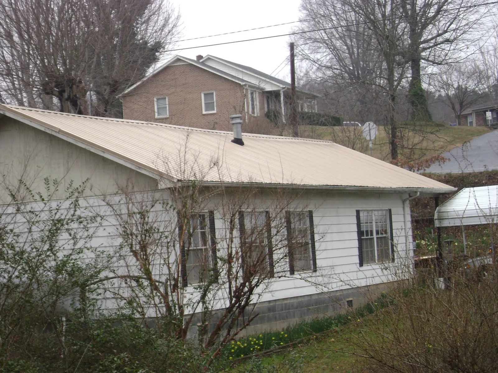 Tan metal roof on a white sided house set into a hillside — Commercial Roofing by Roofing Brothers in Palisades Park